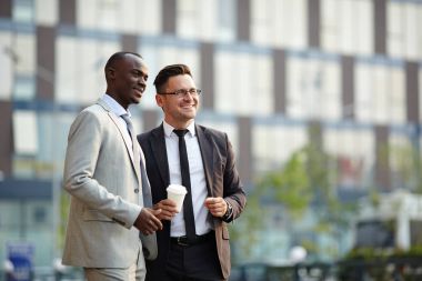 Orta yaşlı işadamı ve Afrika kökenli Amerikalı meslektaşı uzak duran modern ofis binasında geniş gülümsüyor ile seyir