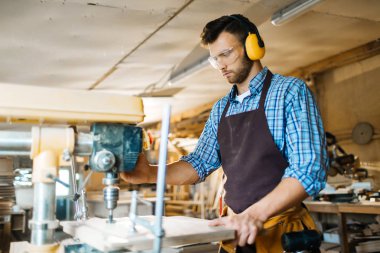 Pansiyon matkap basın, yardımı ile delik yaparken genç woodworker giyen kulak ve göz koruyucular profil görünümü