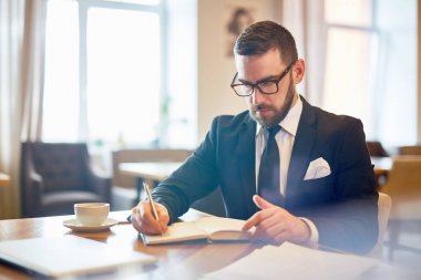 Cafe masa başına oturmuş ve not defterinde yazılı elbiseli yönetmen ya da ceo meşgul