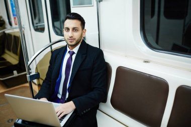 Metro tren, laptop ile çalışma ve kameraya bakarak başarılı Orta Doğu işadamı portresi
