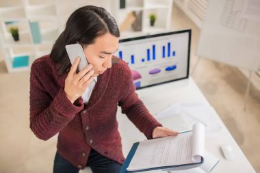 Örme Hırka mali rakamlar üstünde hareket eden telefon, zemin üzerine modern ofis iç meslektaşı ile tartışırken konsantre Asya Yöneticisi yüksek açılı görünüş