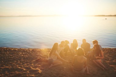 Deniz kenarında kamp ateşi etrafında toplanan çeşitli gençler