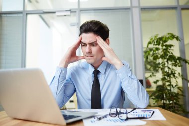 Dizüstü bilgisayar, iç arka plan üzerinde geniş Office Yardımı ile yıllık hesapları hazırlarken korkunç baş ağrısı acı yorgun genç Mali İşler Müdürü