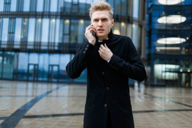 İş ortağı smartphone duran modern cam ofis binası, portre vurdu, konuşurken paltolu yakışıklı girişimci sarılmış