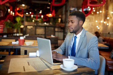 İş giyen emin Afrikalı-Amerikalı adam portresi uygun dizüstü bilgisayar ekranına bakarak kafede masada ile meşgul çalışma