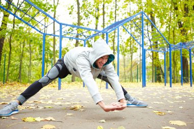 Koşu, sokak egzersiz park arka plan üzerine düşen yapraklar ile önce germe egzersizleri yapıyor sportif genç adam
