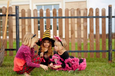 Three girls in traditional halloween costumes playing in the yard by fence clipart