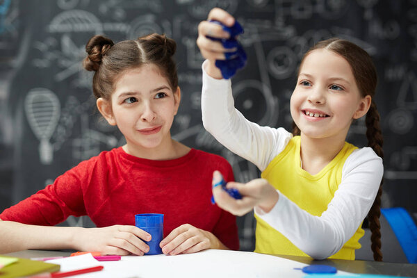 Portrait of two little girls playing with colored plasticine during art class, enjoying feeling and forming it