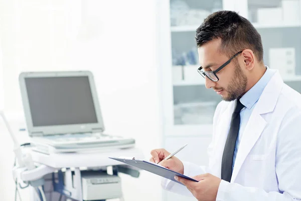 Visão Perfil Jovem Médico Bonito Óculos Preenchendo Cartão Médico Enquanto — Fotografia de Stock