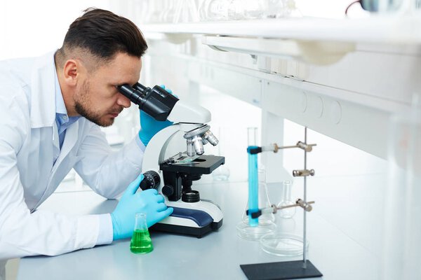 Portrait of handsome scientist using microscope in laboratory while working on important medical research inventing drugs