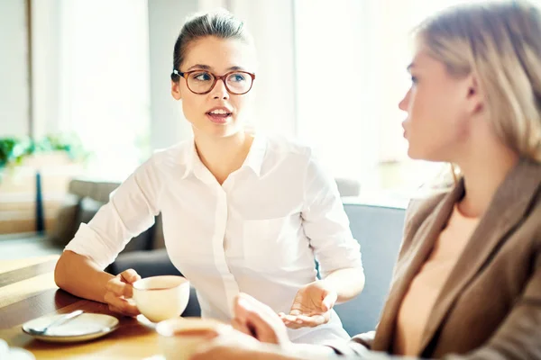 白いシャツとカフェでお茶をしながら友人や同僚の彼女の考えを説明する眼鏡でかわいい女の子 — ストック写真