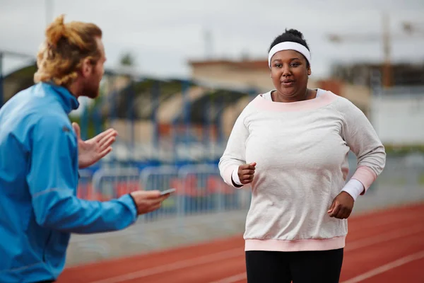 肥胖的年轻女子在运动服接近终点线 而教练给她的建议 保持呼吸 — 图库照片