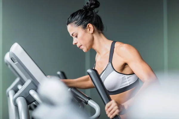 汗合适的女人 行使在现代健身房的高强度锻炼期间使用椭圆机的侧面视图肖像 — 图库照片