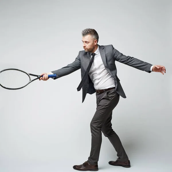 Grauhaariger Geschäftsmann Mittleren Alters Anzug Imitiert Tennisspiel Vor Grauem Hintergrund — Stockfoto