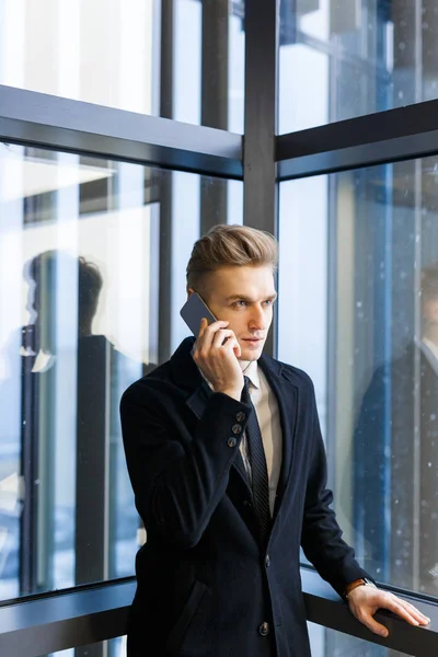 集中年轻的企业家在时髦的西装交谈 他的客户在智能手机 而站在全景窗口 肖像拍摄 — 图库照片