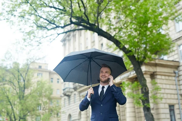 带雨伞的移动代理在智能手机上与客户交谈 — 图库照片