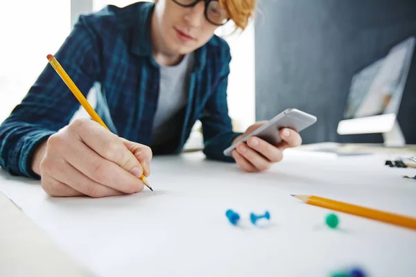 年轻创意红头发男子特写肖像绘图和使用智能手机在办公桌上 专注于手持铅笔 — 图库照片