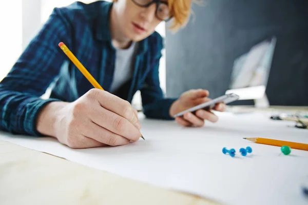 若い創造的な赤髪の男の描画とデスクで鉛筆を持っているクローズ アップ手に焦点を当てるは スマート フォンを使用の肖像画 — ストック写真
