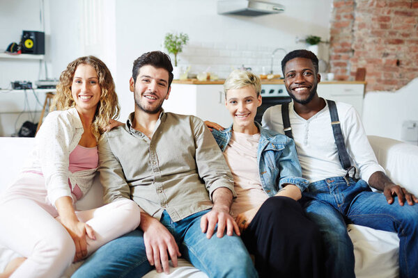 Two young restful couples sitting on sofa while gathering after work or on weekend