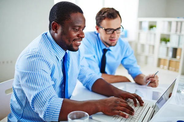 两个男性同事在工作中全神贯注 他们坐在电脑前 分析统计数据 用图表放在办公桌上的文件 — 图库照片