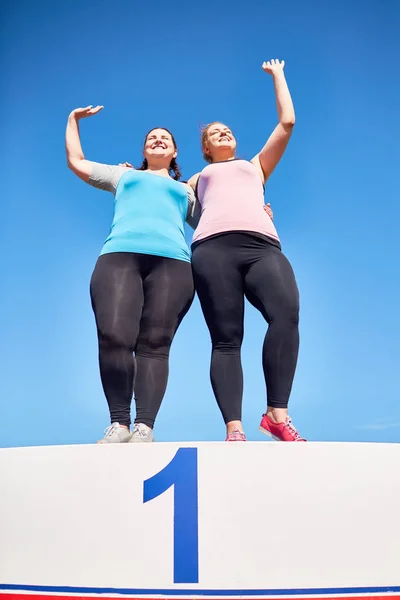 两个大号的妇女站在领奖台上与头号和问候球迷 — 图库照片
