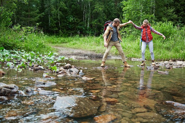 Young man giving his girlfriend helping hand while crossing river
