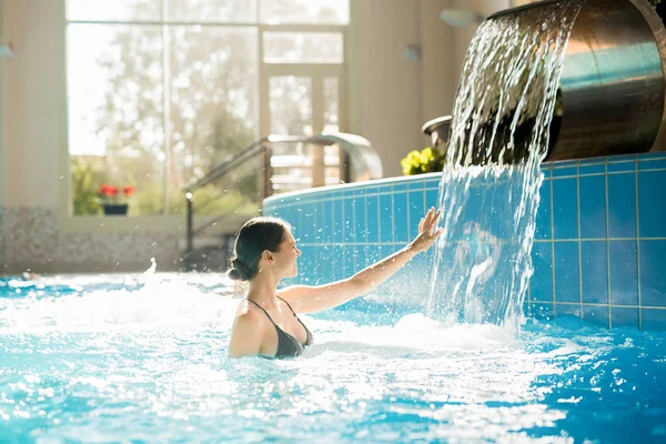 日スパ リゾートのプールで水浴びを楽しみながら滝に触れて恍惚とした女性 — ストック写真