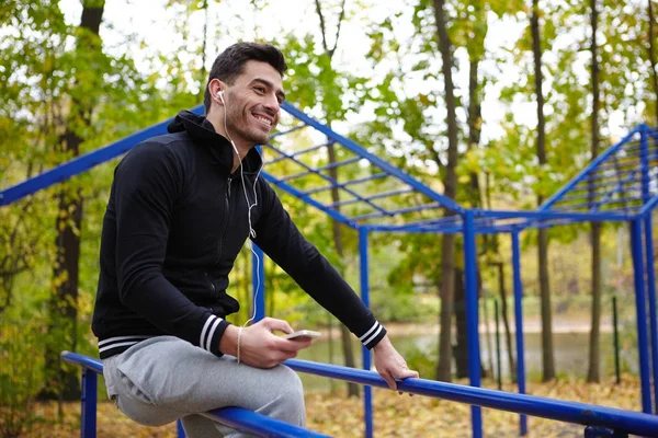 Jovem Desportista Alegre Fones Ouvido Sentado Bares Paralelos Parque Outono — Fotografia de Stock