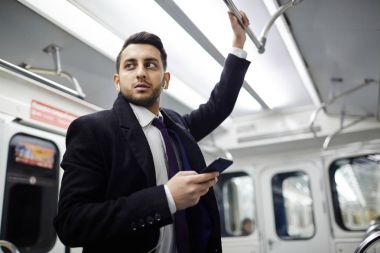 El demiryolu tutarak ve smartphone--dan müzik metro treninin ayakta yakışıklı Ortadoğu işadamı portresi düşük açılı