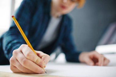 Genç modern kırmızı saçlı mimar planları çalışma masasında erkek eli kalemle kağıt üzerine çizim odaklanmak eğilerek closeup portresi