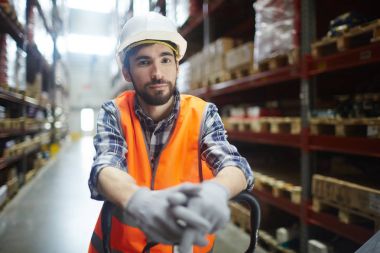 İşçi üniformalı forklift raflar boyunca bastırıyor
