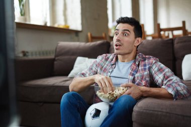 Duygusal adam izlerken futbol maç Tv ve geniş gözlü ve şok seyir patlamış mısır yemek portresi