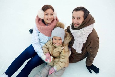 Anne ve kızlarının buz pateni pisti üzerinde otururken kameraya bakarak winterwear içinde