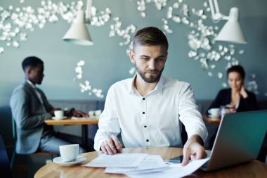 Cafe kahve molası sırasında onun arkasında iki kişi içinde laptop ile çalışırken belgeleri okuma genç sakallı iş adamı portresi