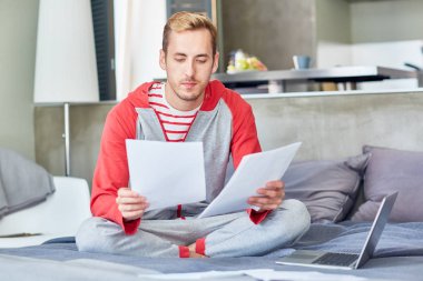Yatakta otururken kağıtları seyir homewear genç adam