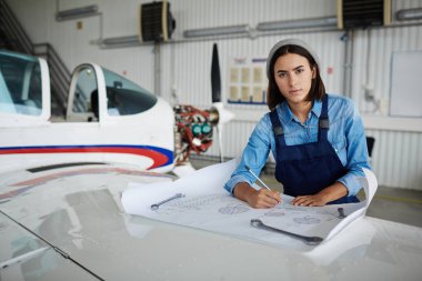 Planları mühendislik ve uçak hangarı kamerada bakarak ile çalışan modern kadın portresi