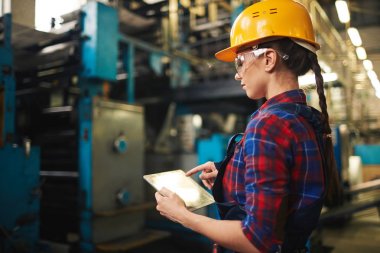 Genç teknisyen endüstriyel makine teftiş ve dijital tablet üzerinde gerekli notlar almak kontrol gömlekli profil görünümü