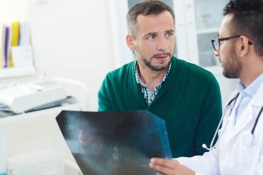 Son derece profesyonel genç Doktor Röntgen sonuçlarını merak hastaya açıklayan ve onu ofisinde randevu sırasında sakinleştirmeye çalışıyor