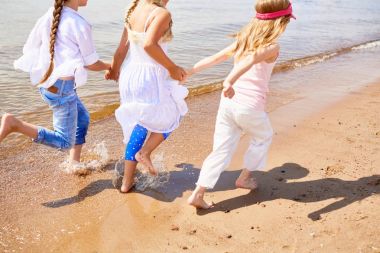 Group of little girls running down sandy beach on summer vacation clipart