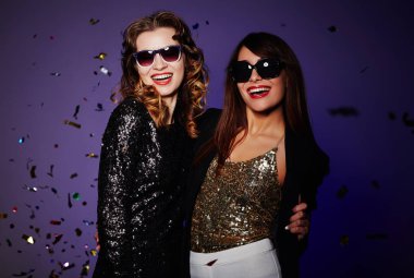 İki neşeli kızlar toplandı birlikte modern gece kulübü ve sevimli gülümsüyor, renkli konfeti arka plan üzerine düşen kamerayla bakarak BT