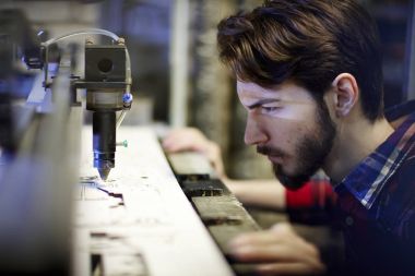 Genç makinist çalışma lazer ışını oyma makine atölyesinde bakarak