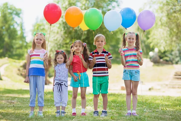 夏服カラフルな風船を公園内の行に立って 押しながらカメラ目線の子供たち — ストック写真