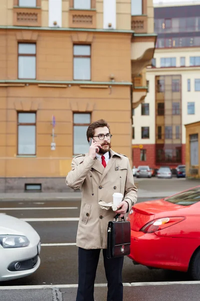 Zajęty Młody Człowiek Piciem Aktówki Mówiąc Smartfonie Podczas Połowu Taksówki — Zdjęcie stockowe