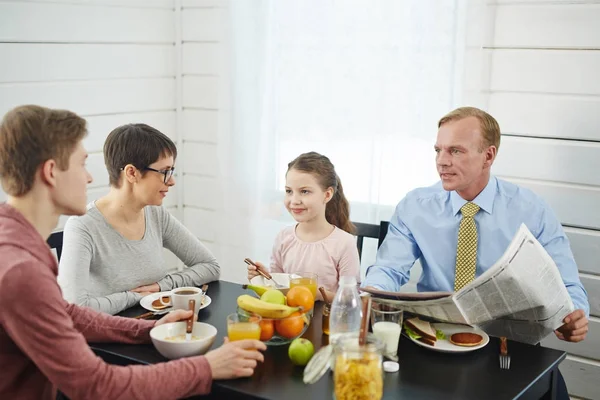 宁静的家庭早餐 Red Haired 的父亲与报纸在手上交谈他十几岁的儿子 小女儿和她的短母亲享受美味的食物 — 图库照片