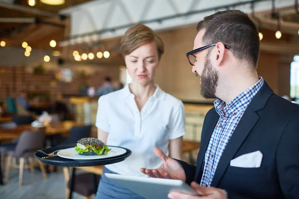 Waitress with tray bringing to businessman with tablet ordered sandwich for lunch