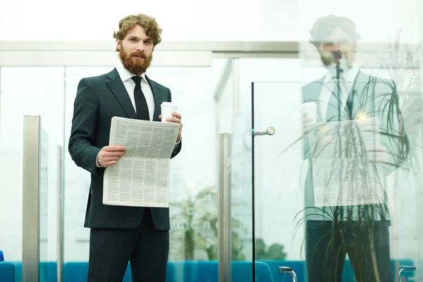 ハンサムなひげを生やしたビジネスマンのオフィスで新聞を押しながらカメラ目線の肖像画 — ストック写真