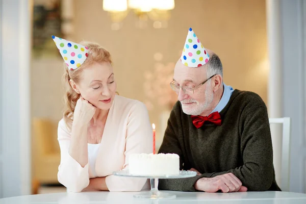 已婚夫妇坐在餐桌旁 在生日蛋糕上看着火的蜡烛 — 图库照片