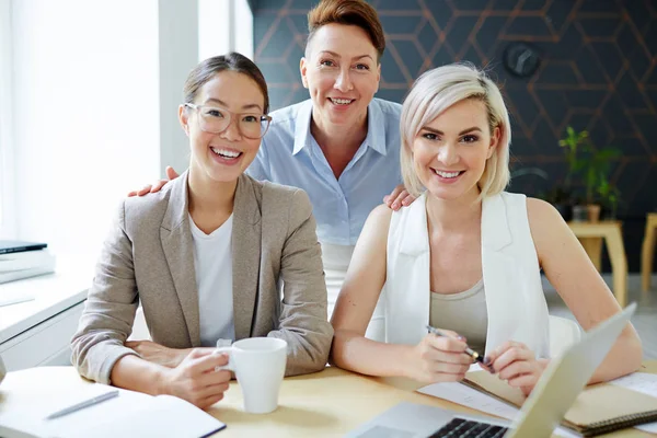 Equipe Empresárias Felizes Sentadas Lado Mesa Escritório Olhando Para Câmera — Fotografia de Stock