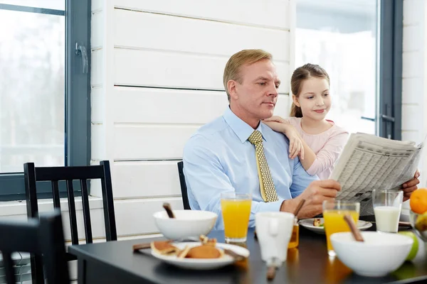 ウエスト アップ肖像画のダイニング ルームで美味しい朝食をとりながら新聞記事を読むに包まれて金髪の中年男と彼のかわいい娘 — ストック写真