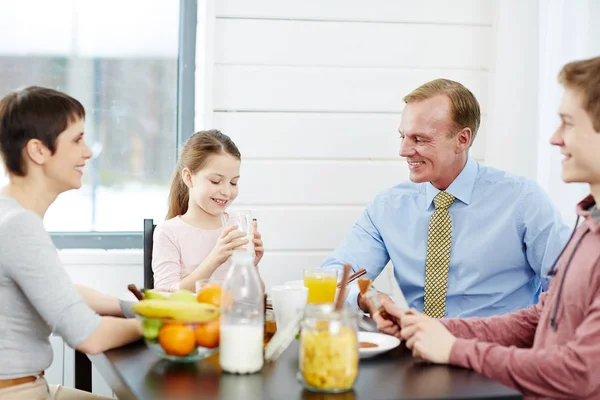 ダイニング テーブルの周りに座って かわいい女の子ガラスから牛乳を飲んで健康的な朝食を楽しんで素敵な家族 — ストック写真